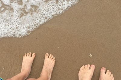 two pairs of bare feet standing on sand and ocean water